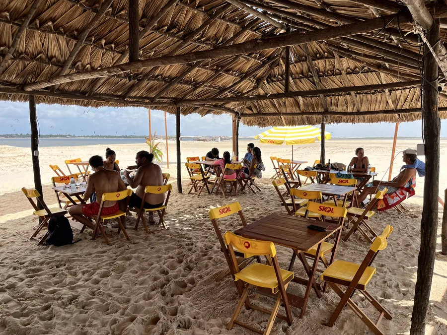 A Cabana do Caranguejo: mesas sob a palha, gente almoçando e a praia ao fundo