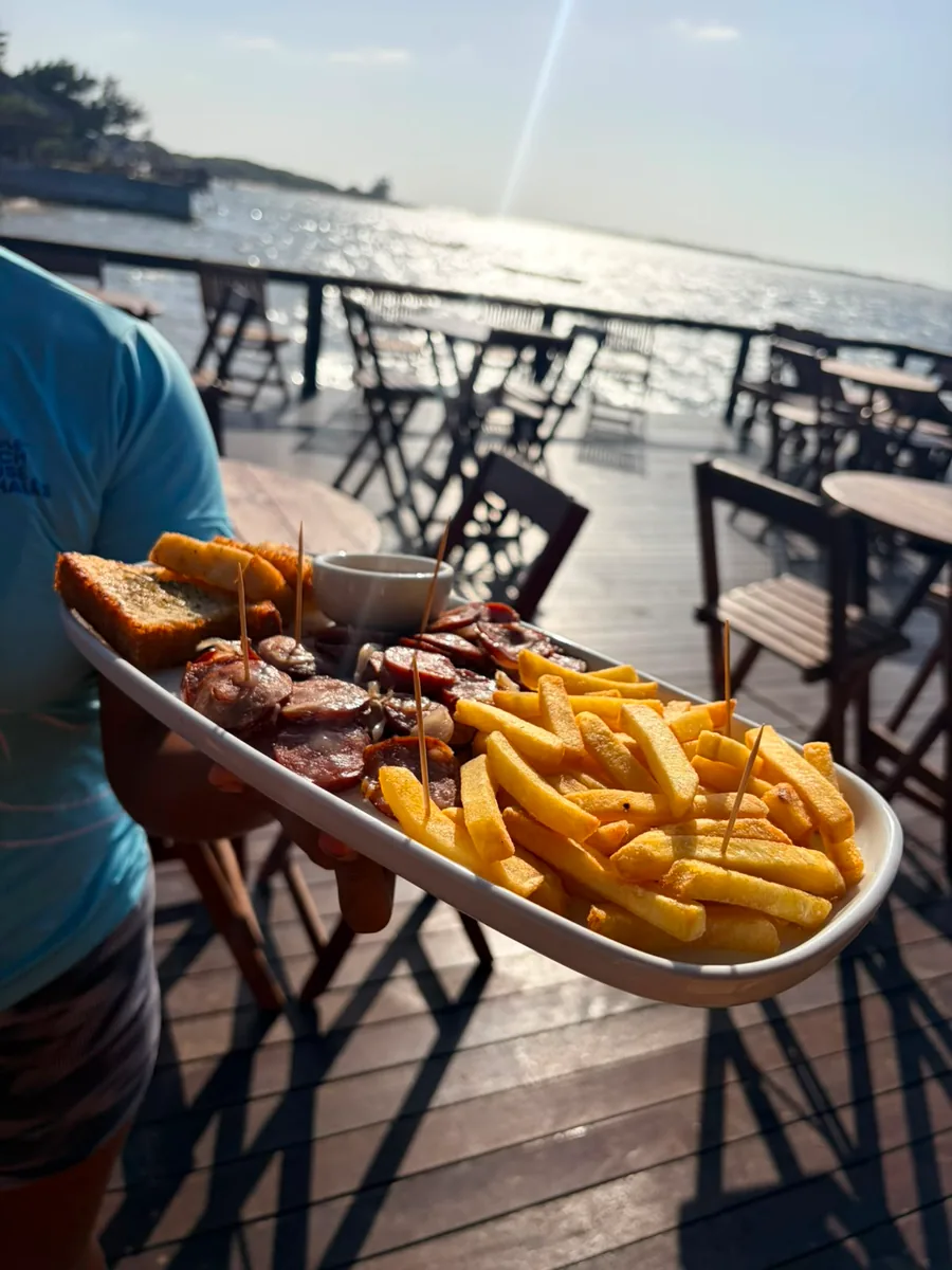 A plate of calabresa sausage with onions and fries, on a table at the Deck facing the sea